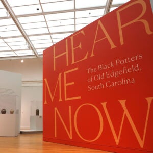 Entrance to the Hear Me Now exhibit at the University of Michigan Museum of Art, featuring a wall-sized graphic of the exhibit title with exhibit showcases visible in the distance.