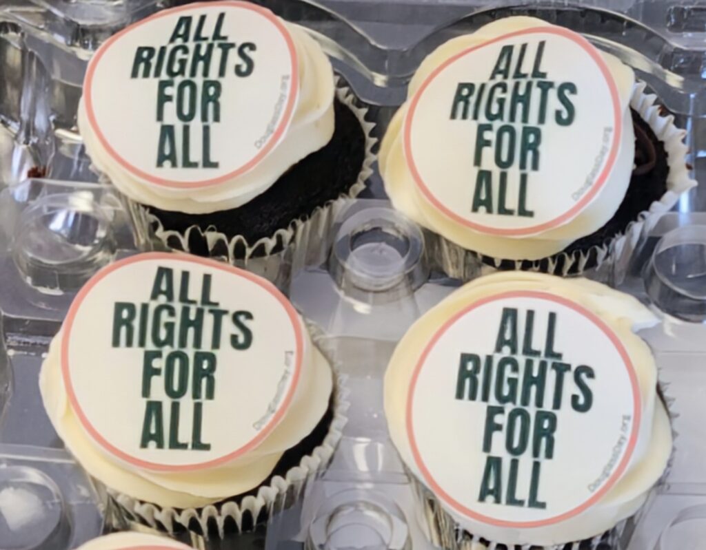 Four chocolate pistachio cupcakes, with a round decoration that reads "All Rights for All"